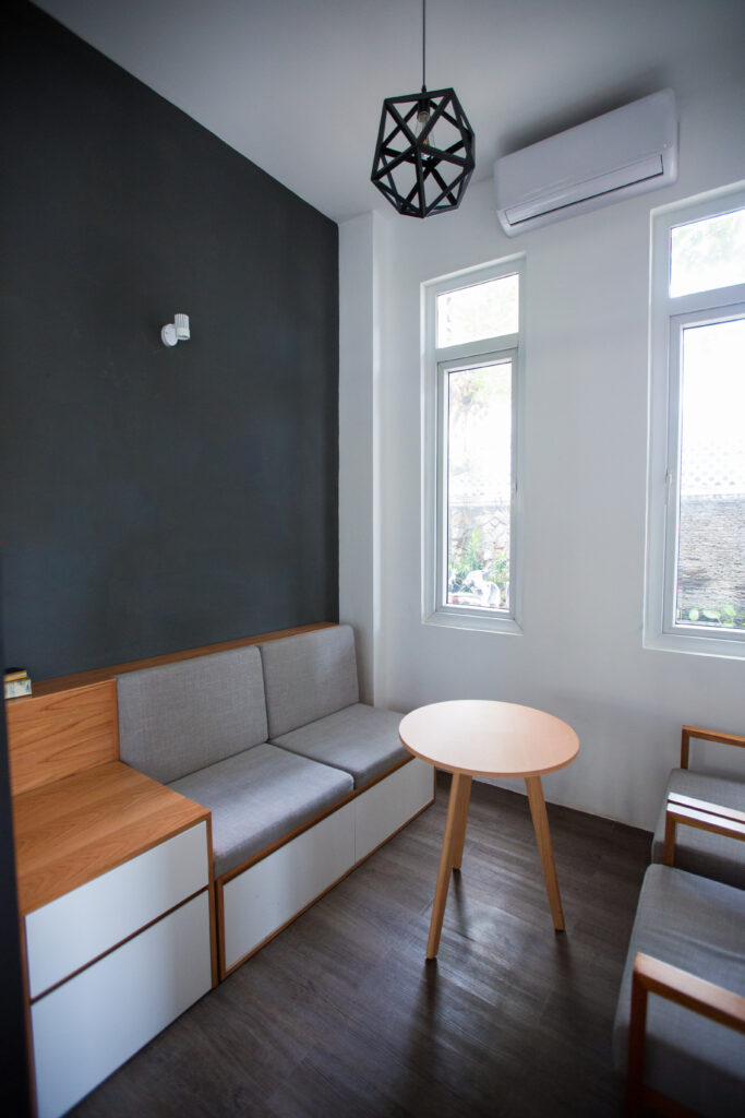 Modern gray design of small room with air conditioner and light fixture in shape of polygon. Sofa with small cabinet against wall, coffee table in center of room. Home interior concept